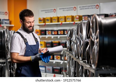 männlicher Verkäufer im Autoshop, der Notizen macht, das Dokument überprüft und die Eigenschaften überprüft, Rack mit Auto-Riemen betrachtet