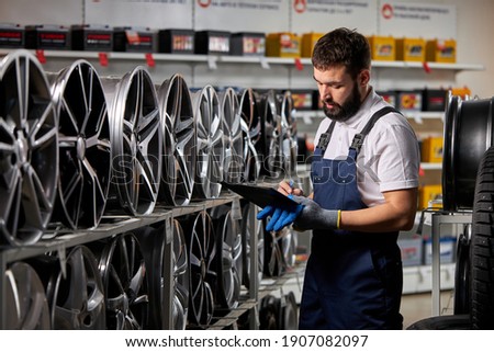 male salesman in auto shop making notes, checking the document and examining characteristics, looking at rack with auto rims