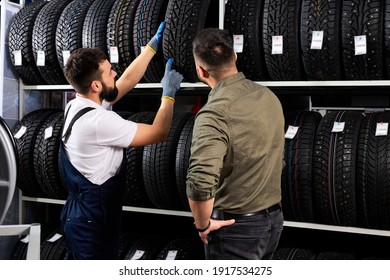male salesman showing wheel tires to caucasian man customer at car repair service and auto store shop, they are discussing and talk about advantages of tires