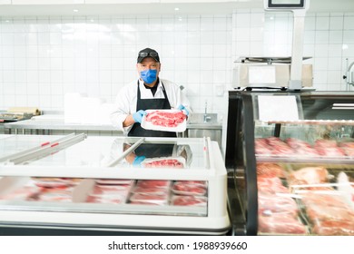 Male Salesman Using A Face Mask While Working At A Butcher Shop. Portrait Of A Worker At The Supermarket Selling Raw Meat 