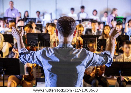 Male school conductor conductiong his student band to perform music in a school concert