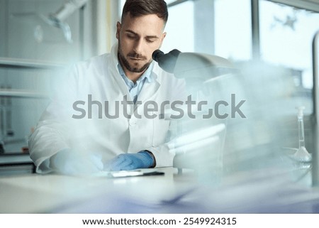 Male scientist taking notes while working on microscope in laboratory.