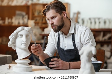 Male sculptor repairing gypsum sculpture of woman's head at the working place in the creative artistic studio. - Powered by Shutterstock