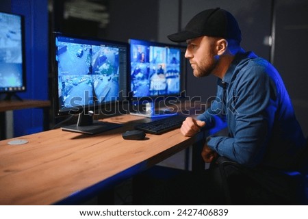 Male security guard monitoring modern CCTV cameras indoors.