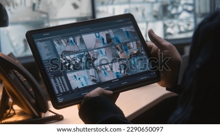 Male security officer controls CCTV cameras in office, uses digital tablet and computers with surveillance camera footage playback on screens. High tech security system. Monitoring and social safety.