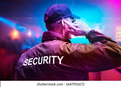 Male Security Officer Wearing Cap Trying To Listen Something On Earphones In Night Club