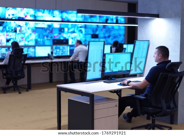 Male security operator working in a data system\
control room offices Technical Operator Working at  workstation\
with multiple displays, security guard working on multiple monitors\
 Male computer opera