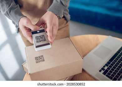 Male seller aiming his camera at the QR code on the cardboard box