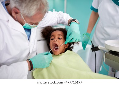 Male Senior Dentist Repairing Black Kid's Tooth