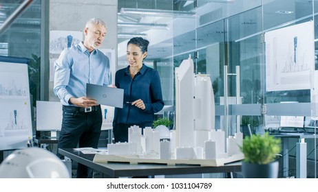 Male Senior Engineer Holds Laptop and has Discussion with Female Chief Engineer. They Work on a Building Model for a New District Urban Planning Project. - Powered by Shutterstock