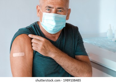 Male Senior In Face Mask After Receiving COVID-19 Vaccine. Elderly Man Feeling Good On Getting Coronavirus Vaccine. Covid Vaccination For Older People. Senior Patient Showing Arm With Bandage, Patch.