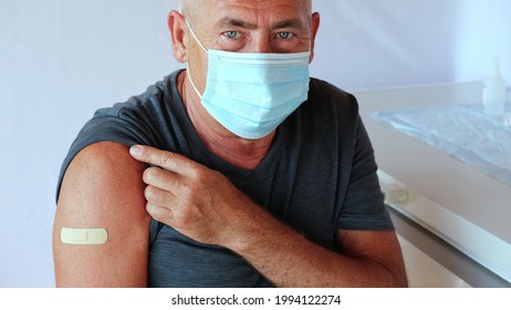 Male Senior In Face Mask After Receiving COVID-19 Vaccine. Elderly Man Feeling Good On Getting Coronavirus Vaccine. Covid Vaccination For Older People. Senior Patient Showing Arm With Bandage, Patch.