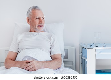 Male Senior Patient Relaxing In Bed In Hospital Ward While Looking In Window