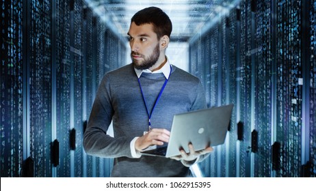 Male IT Server Technician Specialist Holds Laptop and Looking on Raining Script Code in Rack Sever Cabinet. He is Standing in Data Center. - Powered by Shutterstock