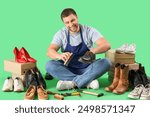 Male shoemaker brushing boot on green background