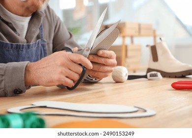 Male shoemaker cutting insole at table in workshop, closeup - Powered by Shutterstock