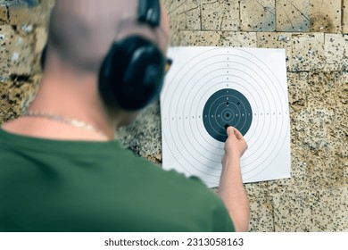 Un tirador masculino cerca del objetivo en el campo de tiro marca los agujeros de las balas.