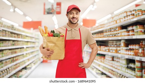 Male Shop Assistant With Food In A Paper Bag Standing Inside A Supermarket