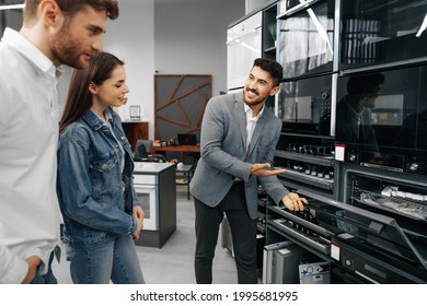 Male Shop Assistant Helps Young Couple To Choose New Home Appliance