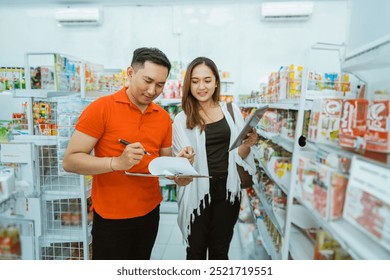 male shop assistant stands writing with clipboard with female business owner at minimarket - Powered by Shutterstock