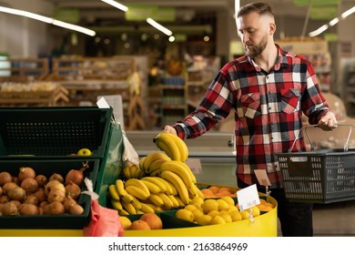 male shopper in the fruit section of the supermarket, man buying bananas in the grocery store, organic fruits, shopping concept