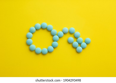 Male sign with bent arrow of blue pills symbolizing potency problems on yellow background, flat lay