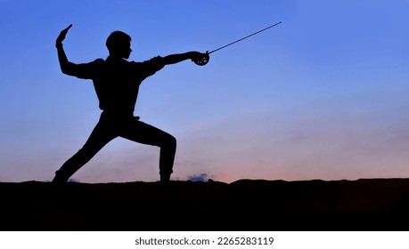 Male silhouette against the blue sky.  A man with a rapier in his hands is engaged in fencing. - Powered by Shutterstock