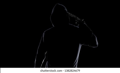 Male silhouette in hoodie with gun attached to his temple, committing suicide