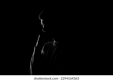 Male silhouette on a black background. A man stands thoughtfully on a black background