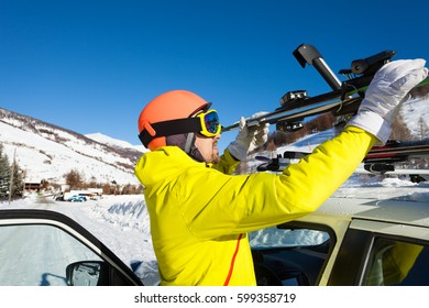 Male Skier Fastening Skis To Roof Rails Of Car