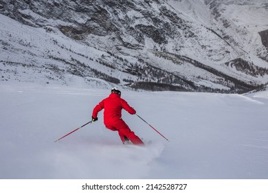 Male skier skiing and carving turn on prepared ski slope at ski resort after taking chairlift on snow-covered mountain. Safety ski descent in high mountains. Ski chairlift on wooded hill on background