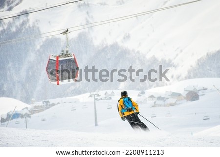 Male skier skiing downhill fast pass cabin lift in snowy conditions to gondola with mountains background. Gudauri winter holiday resort. Georgia travel destination. Caucasus