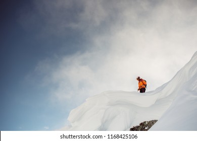 Male skiier standing on top of cliff in the alps looking down at slope before dropping in