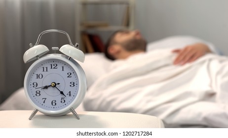 Male Sleeping In Bed, White Alarm Clock Standing On Table Morning, Biorhythm