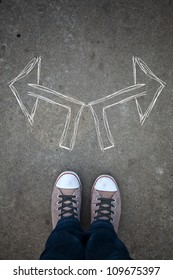 Male Sneakers On The Asphalt Road With Drawn Arrows Pointing To Two Directions. Youth Guidance, Student Guide, Advisory Concept. Making Decisions And Making Choices.