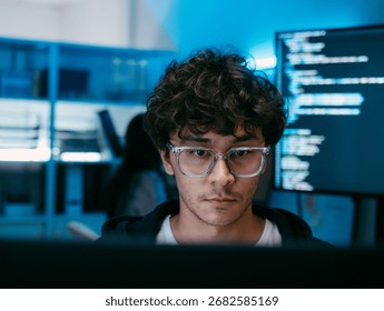 Male Software Engineer, Computer Programmer sits at desk Writing Code on Desktop computer with Dual Screens at Tech Office at Night. Professional Male IT expert working on Software Code and Program.