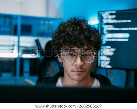 Male Software Engineer, Computer Programmer sits at desk Writing Code on Desktop computer with Dual Screens at Tech Office at Night. Professional Male IT expert working on Software Code and Program.