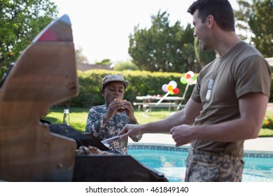 Male Soldier And Boy Barbecuing Burgers At Homecoming Party