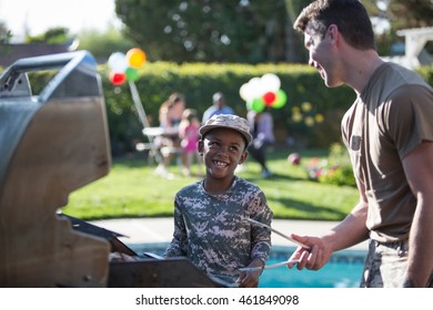 Male Soldier And Boy Barbecuing At Homecoming Party