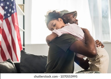 Male soldier in camouflage clothes and her daughter embracing on sofa - Powered by Shutterstock