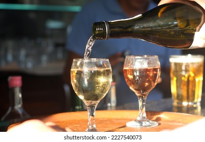 Male sommelier pouring white wine into long-stemmed wineglasses. Waiter with bottle of alcohol beverage. Bartender at bar counter pour elite drink into long-stemmed glass - Shutterstock ID 2227540073