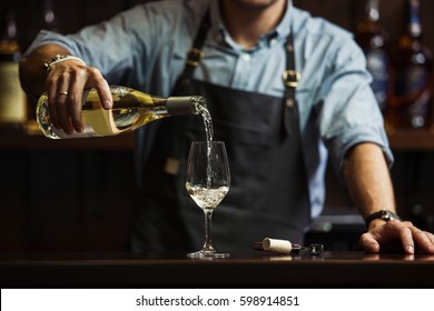 Male sommelier pouring white wine into long-stemmed wineglasses. - Powered by Shutterstock