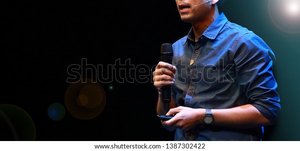 The male speaker is doing the public speaking\
with the dark background under the spot light and lense flare, in\
concept of talk show, flare light, motivational speaking,\
inspiration speaker.