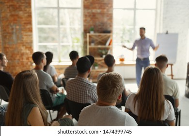 Male speaker giving presentation in hall at university workshop. Audience or conference hall. Rear view of unrecognized participants in audience. Scientific conference event, training. Education