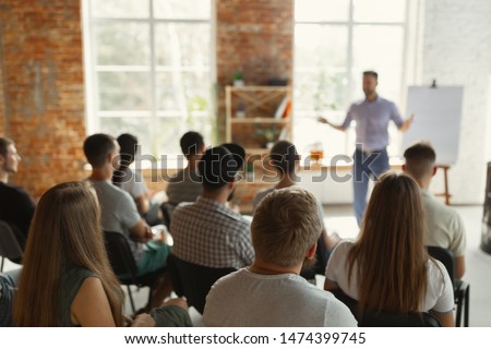 Male speaker giving presentation in hall at university workshop. Audience or conference hall. Rear view of unrecognized participants in audience. Scientific conference event, training. Education