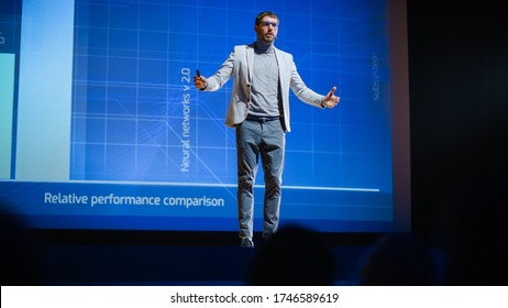 Male Speaker Stands On Stage And Does Presentation Of The Technological Product, Shows Infographics, Statistics Animation On Screen. Live Event / Device Release / Start-up Conference