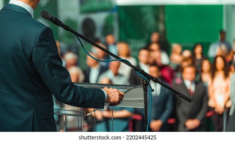 Male speaker wearing suit standing in front of microphones at media press conference. - Shutterstock ID 2202445425