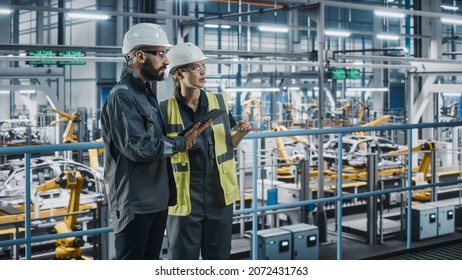 Male Specialist and Female Car Factory Engineer in High Visibility Vests Using Tablet Computer. Automotive Industrial Manufacturing Facility Working on Vehicle Production. Diversity on Assembly Plant.