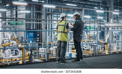 Male Specialist and Female Car Factory Engineer in High Visibility Vests Using Tablet Computer. Automotive Industrial Manufacturing Facility Working on Vehicle Production. Diversity on Assembly Plant. - Shutterstock ID 2072431838