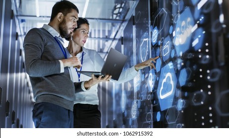Male IT Specialist Holds Laptop and Discusses Work with Female Server Technician. They're Standing in Data Center, Rack Server Cabinet with Cloud Server Icon and Visualization.